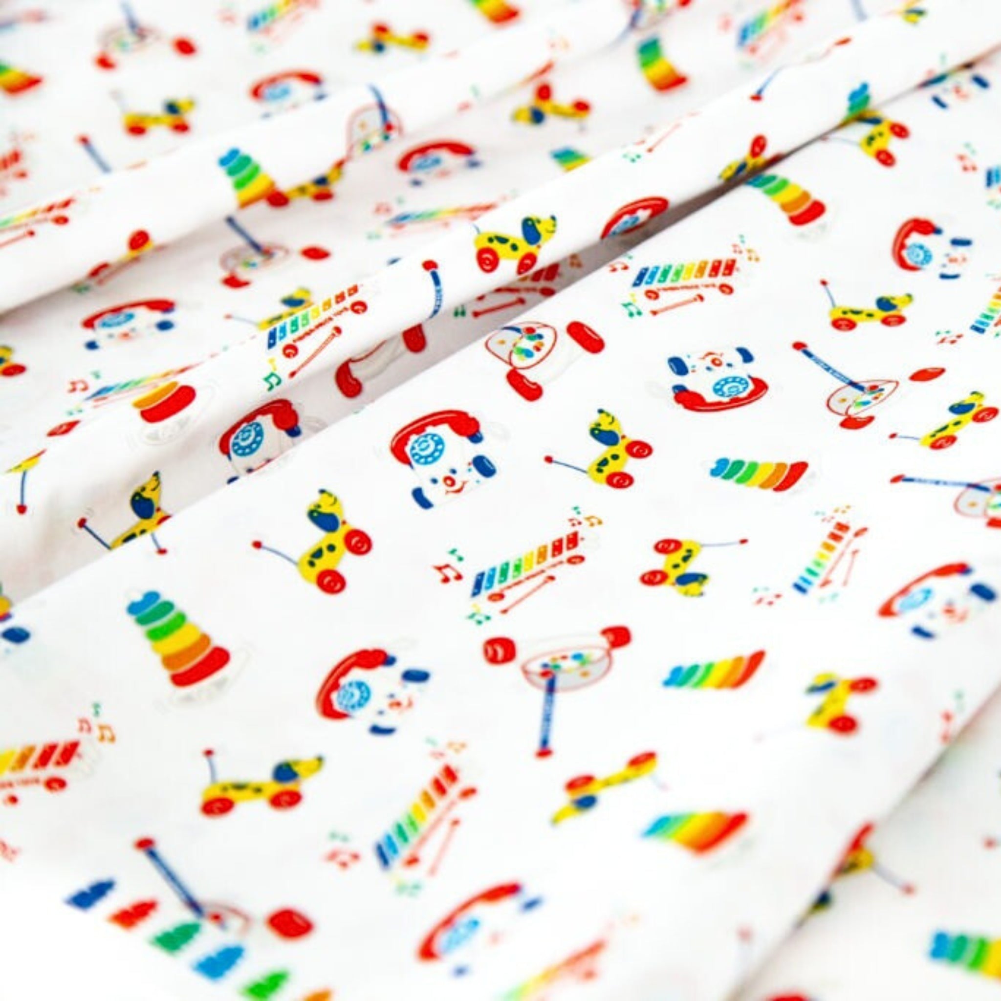 White quilting cotton with bright, tossed Fisher-Price classic toy motifs