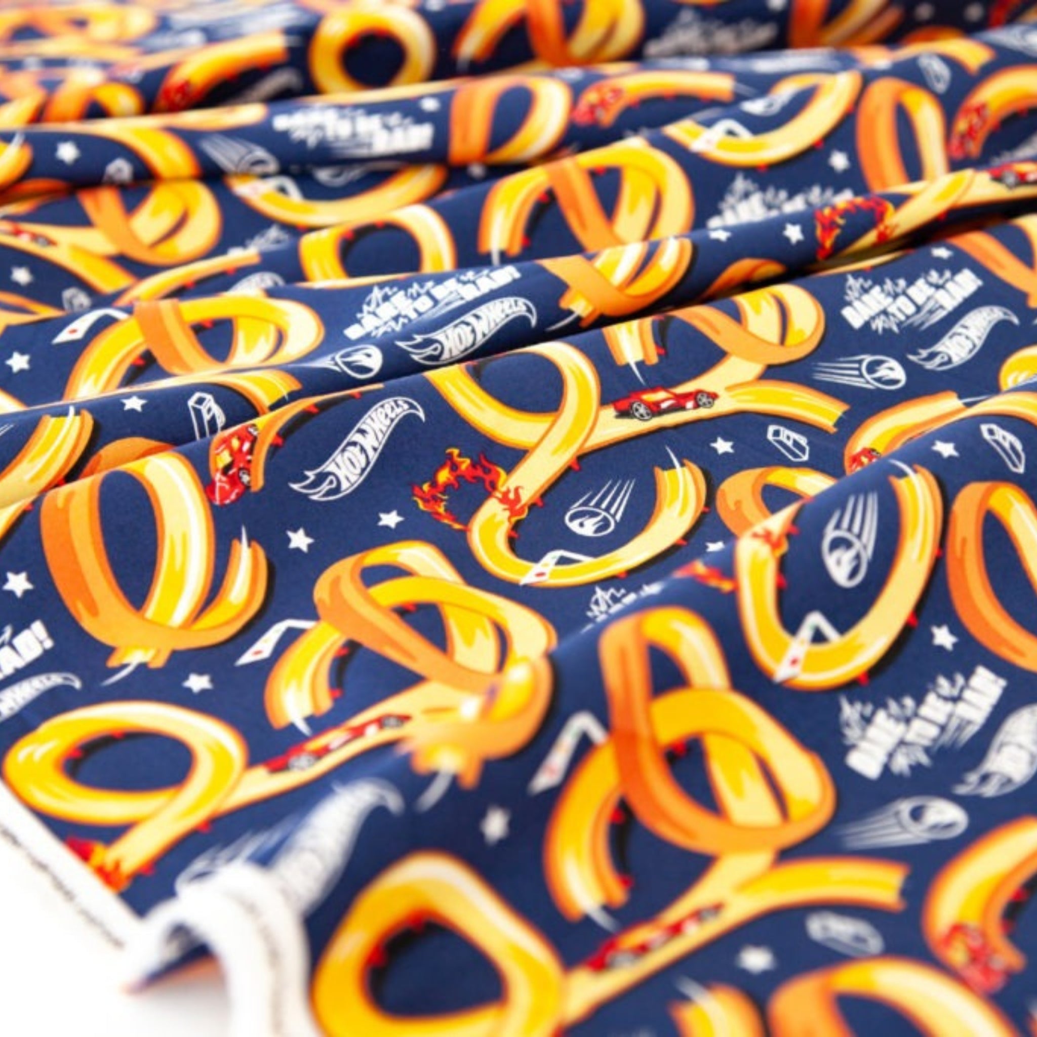Hot Wheels-themed fabric with red race cars on yellow tracks on a navy blue background for boys quilts