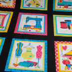 Sewing novelty fabric panel machines dress forms thread spools scissors and pincushions in multicolour blocks on black with quilt label blocks for sewing-themed quilts tote bags and patchwork projects